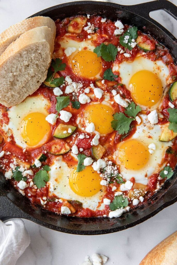 Simple shakshuka with toasted bread and soft poached eggs in a cast iron skillet.