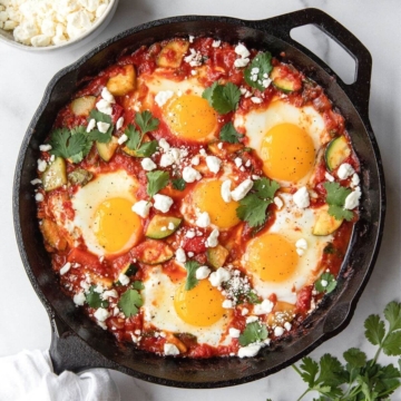 Best ever healthy shakshuka recipe in cast iron skillet with lots of fresh vegetables and crumbled feta.