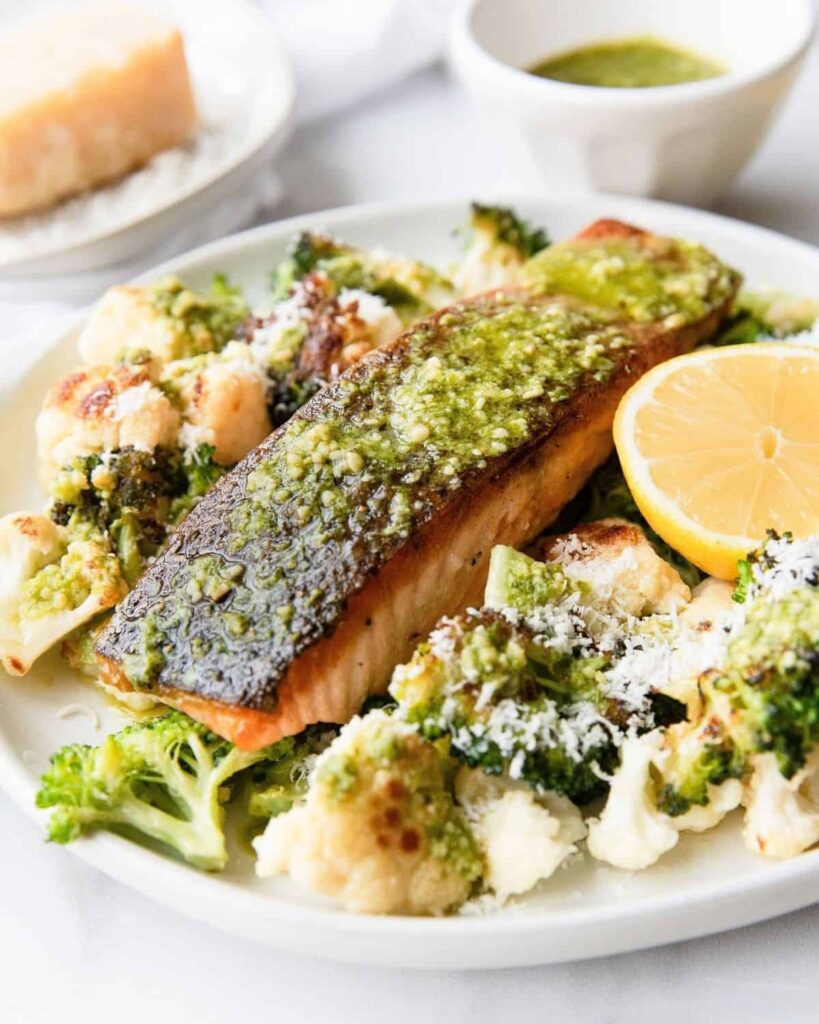 Pesto topped salmon with a side of delicious cheesy roasted vegetables. Ideal meal prep recipe for everyone! Perfect family dinner or date night dinner idea. Ready in 25 minutes! Recipe by Healthful Blondie.