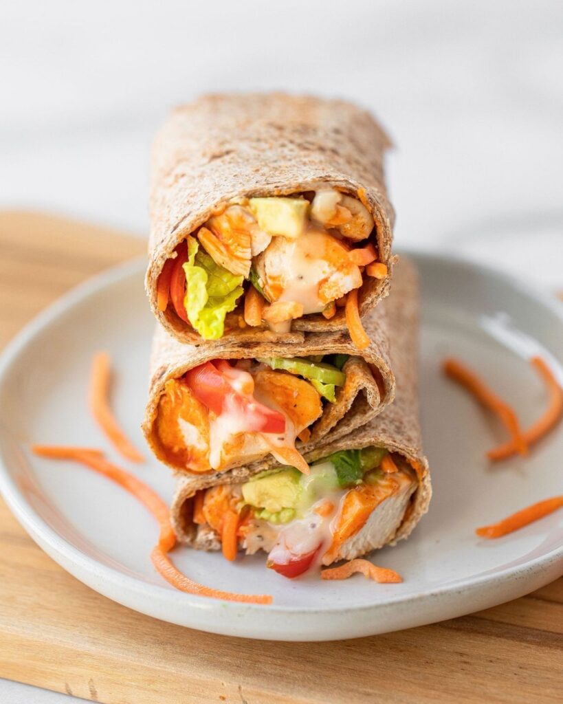 Close up image of buffalo chicken caesar wraps stacked on top of each other. Super easy healthy lunch recipe. Loaded with organic chicken, buffalo sauce, avocado, fresh vegetables, and wrapped in a low calorie whole wheat wrap.