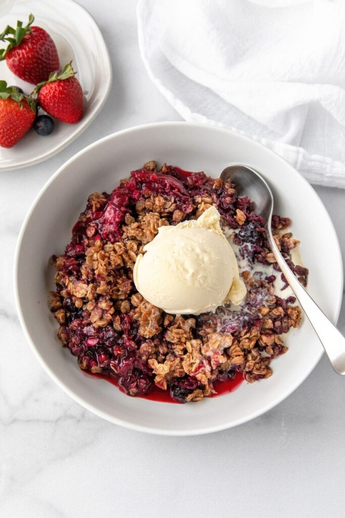 Healthy mixed berry crisp in a bowl with vanilla ice cream on top