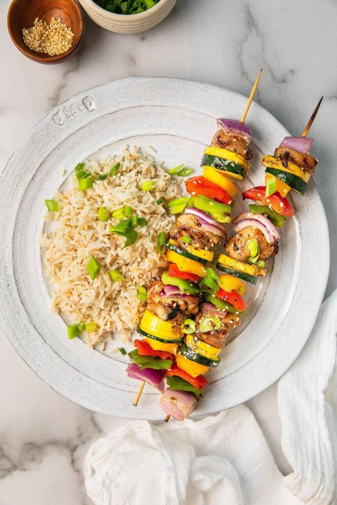 grilled vegetable and chicken thigh skewers on a plate with brown rice