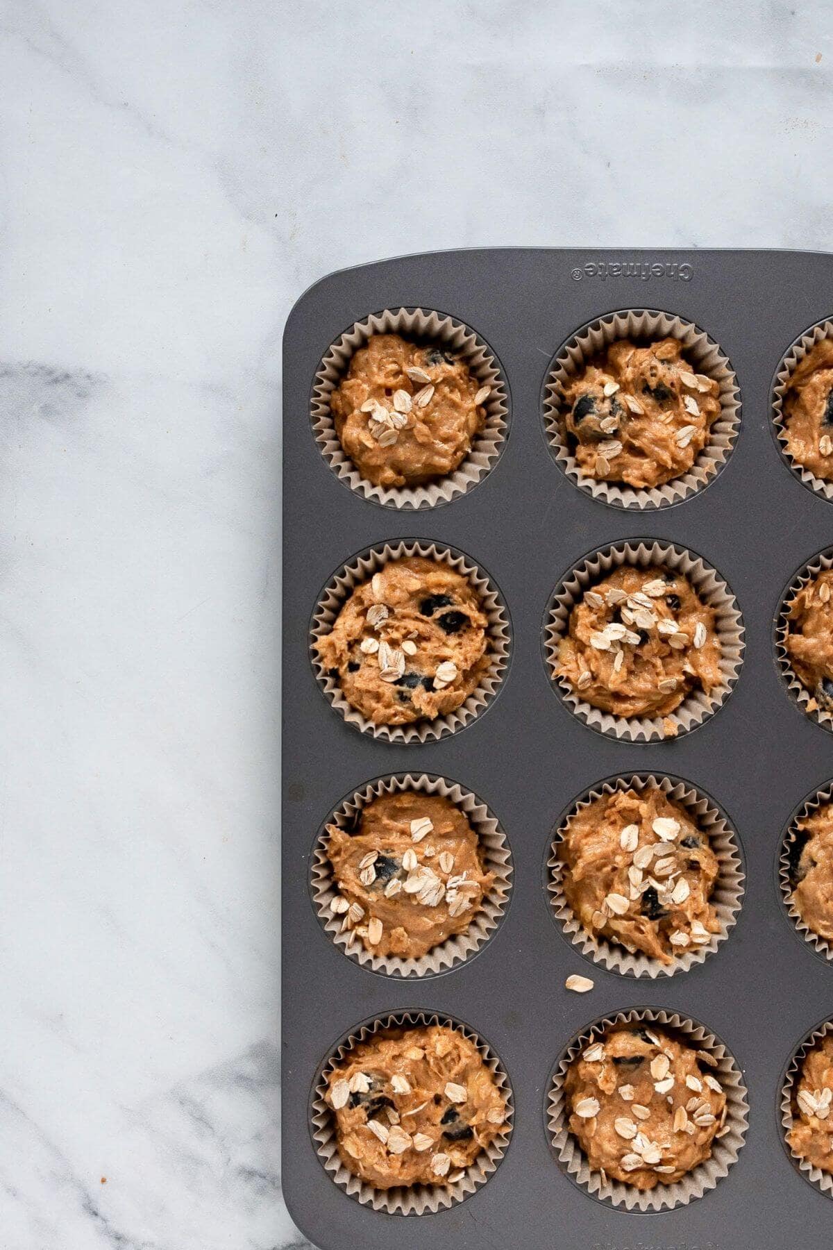 Banana blueberry oatmeal muffin batter divided evenly in a dark muffin tin before baking.