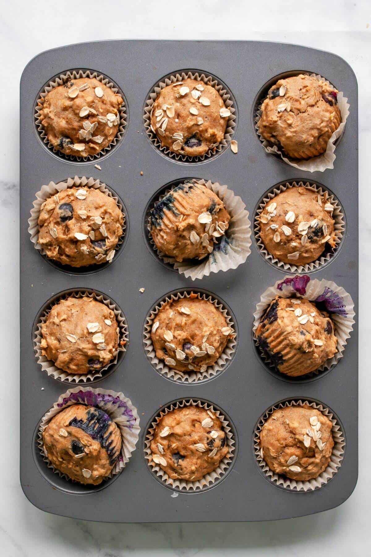 Freshly baked healthy banana blueberry oatmeal muffins cooling in a muffin tin.
