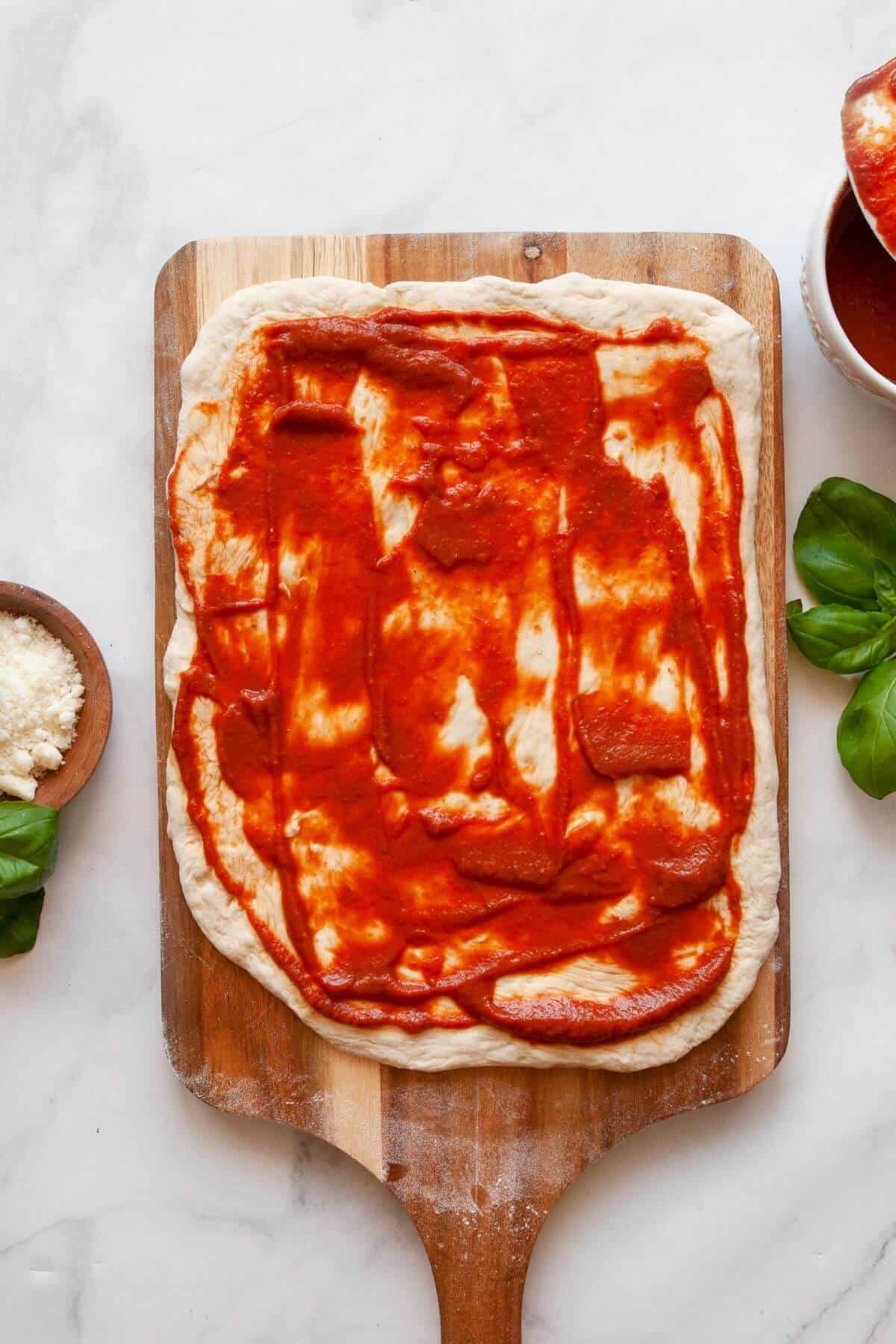 Rolling out pizza dough and spreading marinara sauce for homemade air fryer pizza rolls.