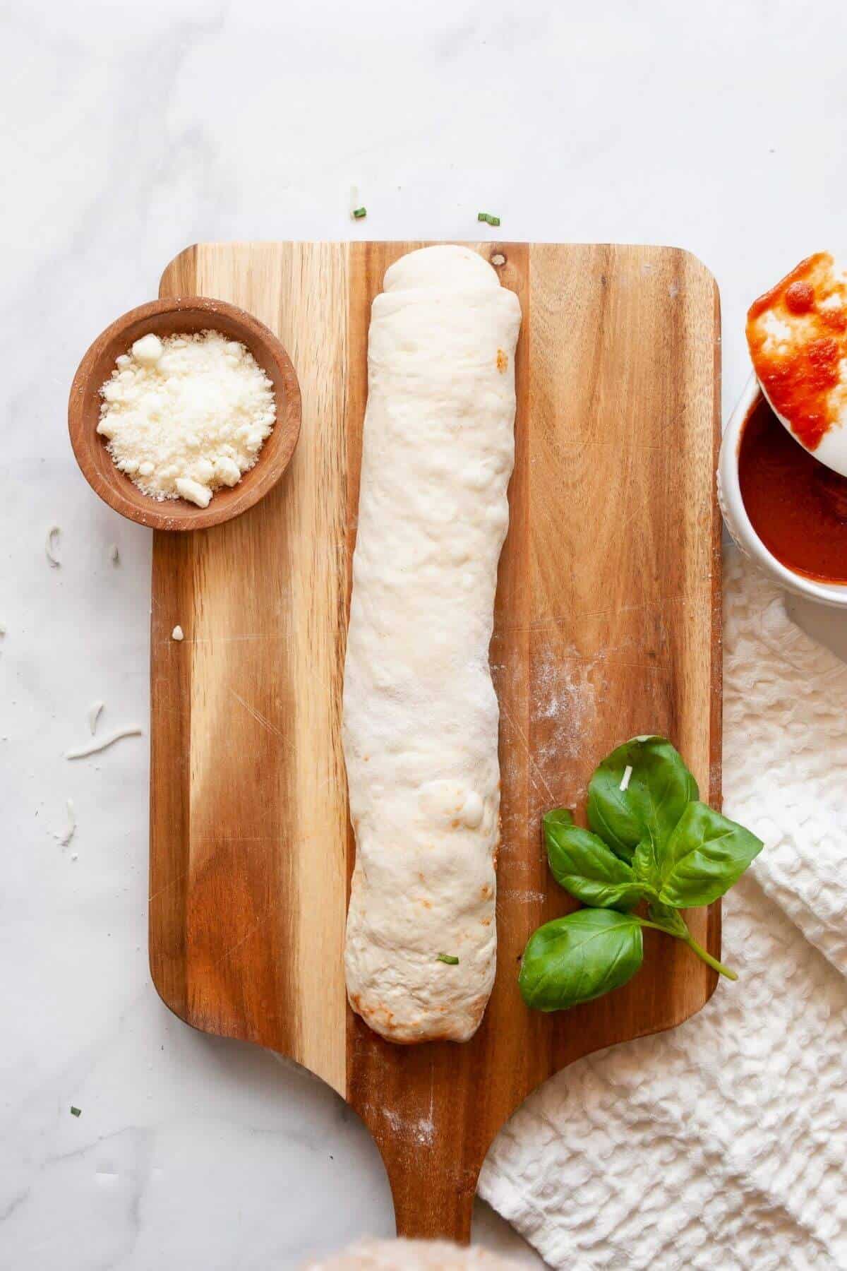 Rolling up pizza dough tightly with mozzarella, marinara, and basil to make homemade air fryer pizza rolls.