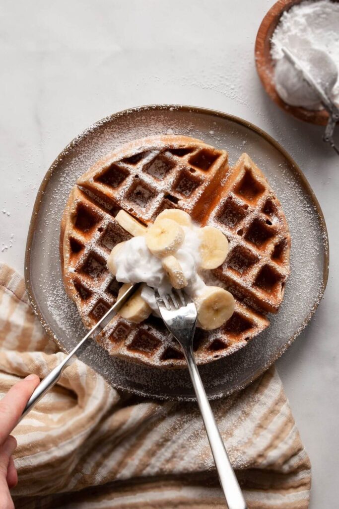 cutting into healthy banana waffles with a fork and knife