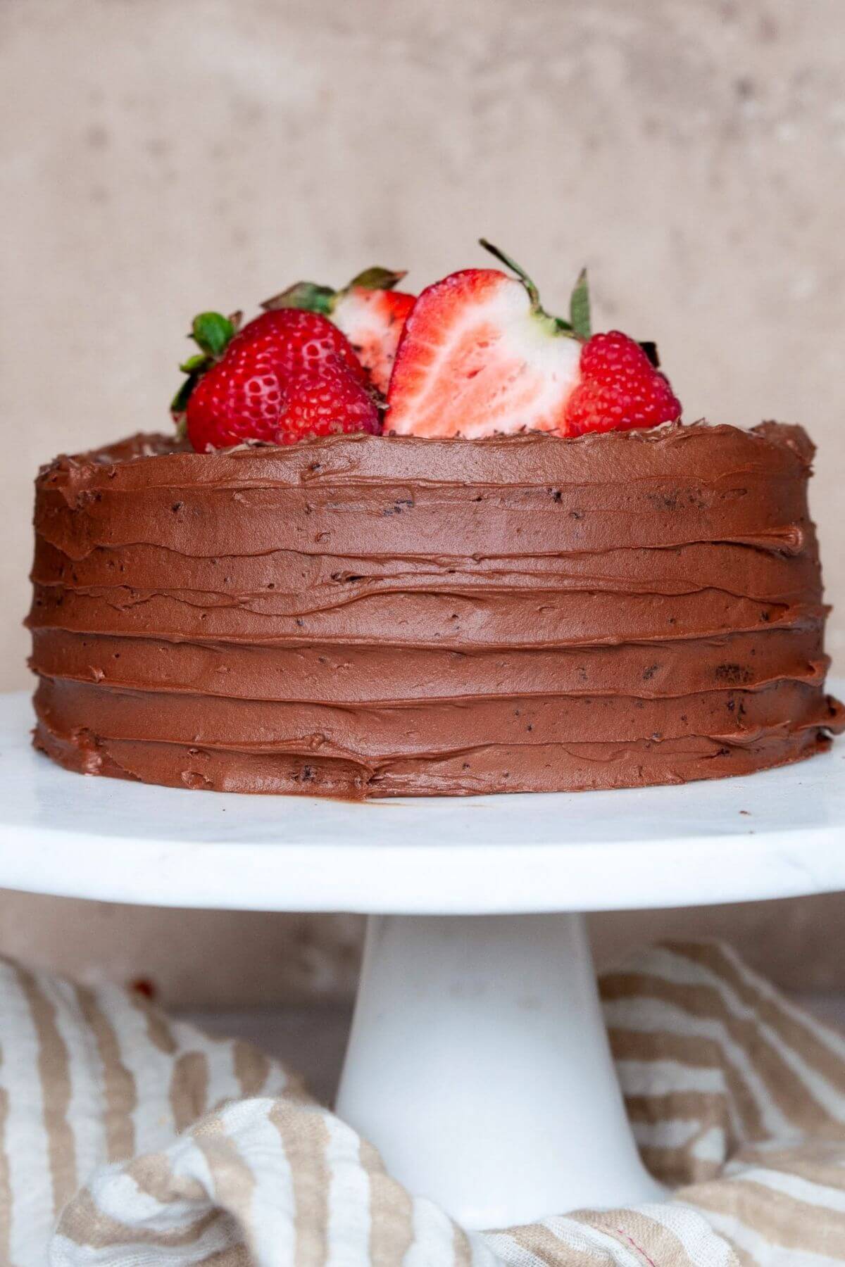 Gluten-free almond flour chocolate cake on a white cake stand with strawberries and chocolate shavings.