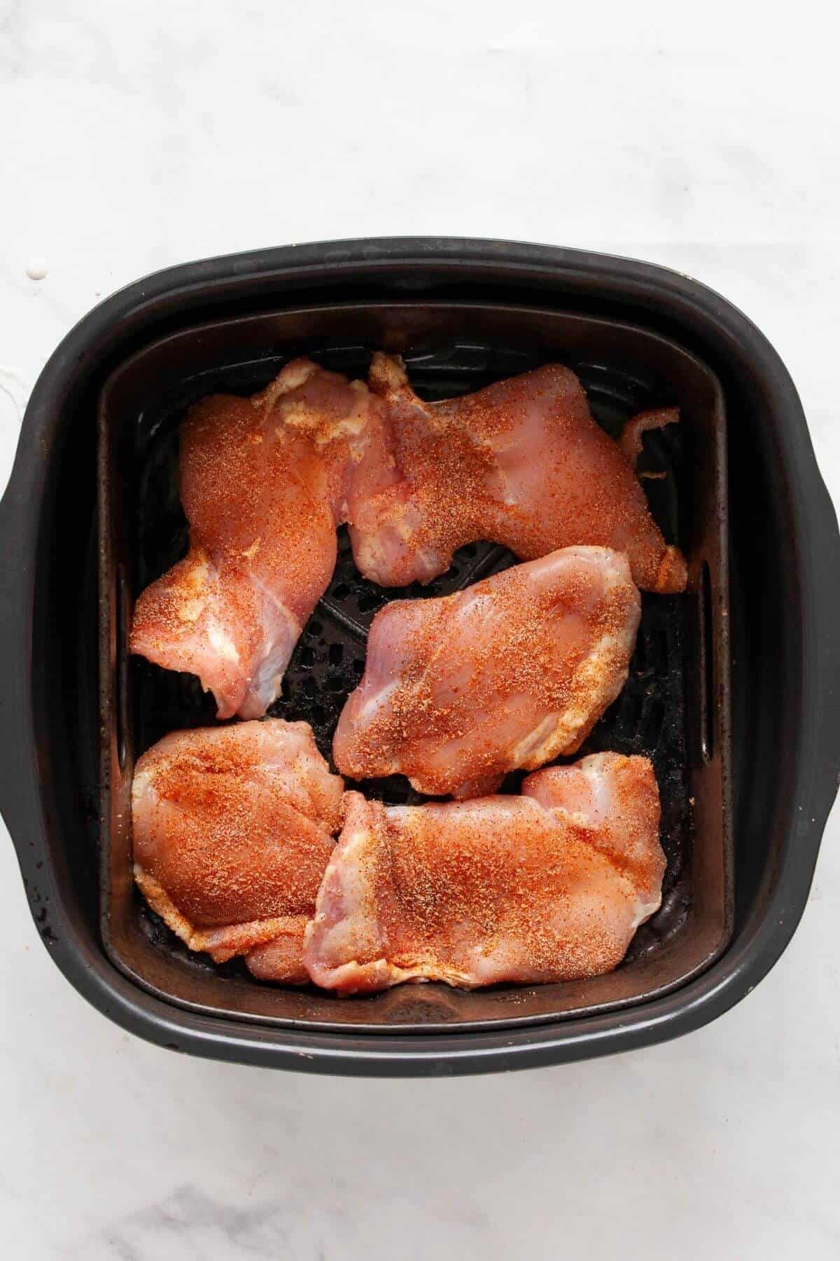Seasoned chicken thighs arranged smooth-side down in an air fryer basket in a single layer.