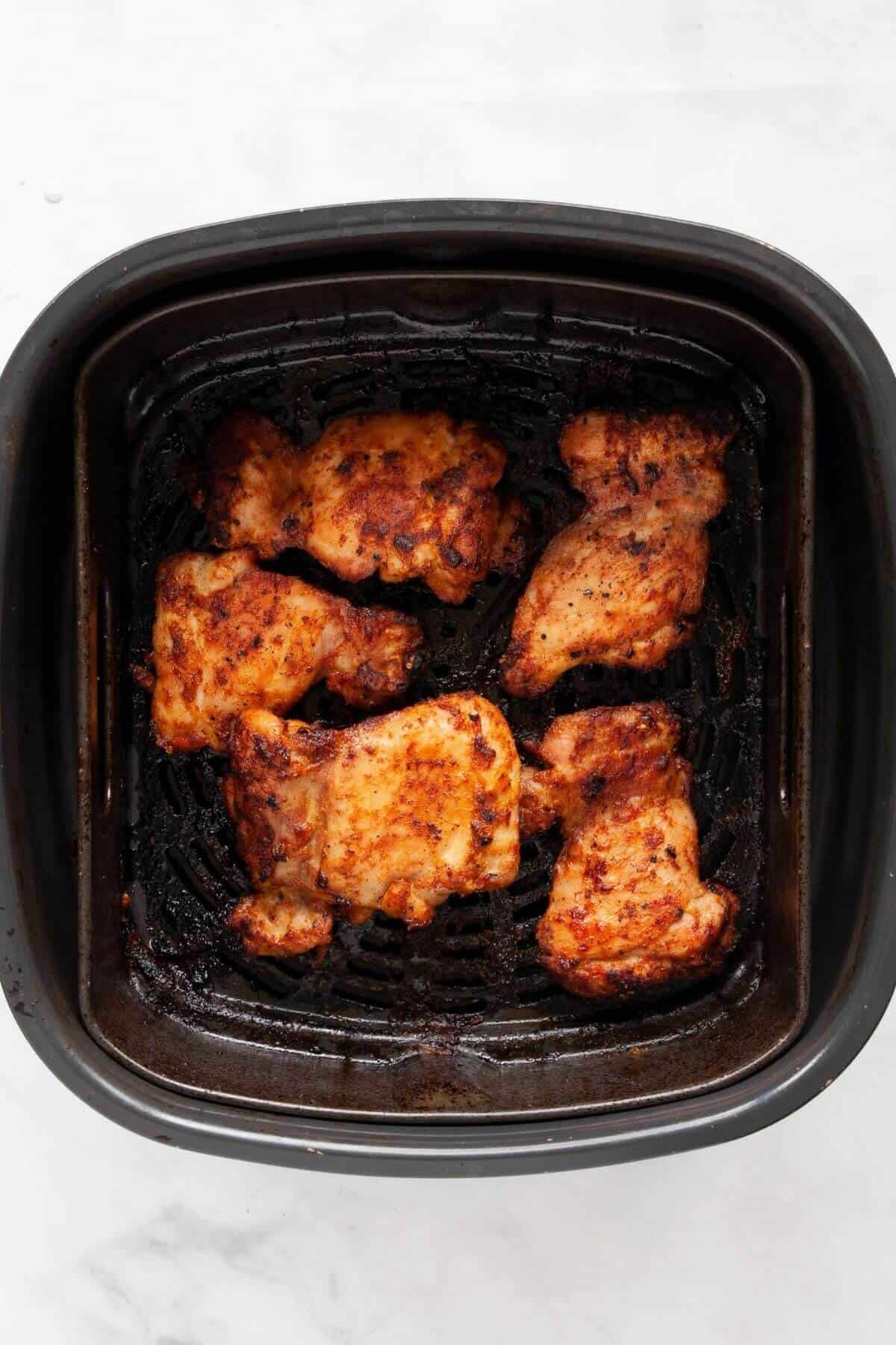 Crispy golden air fryer chicken thighs with browned edges in the air fryer basket after cooking.