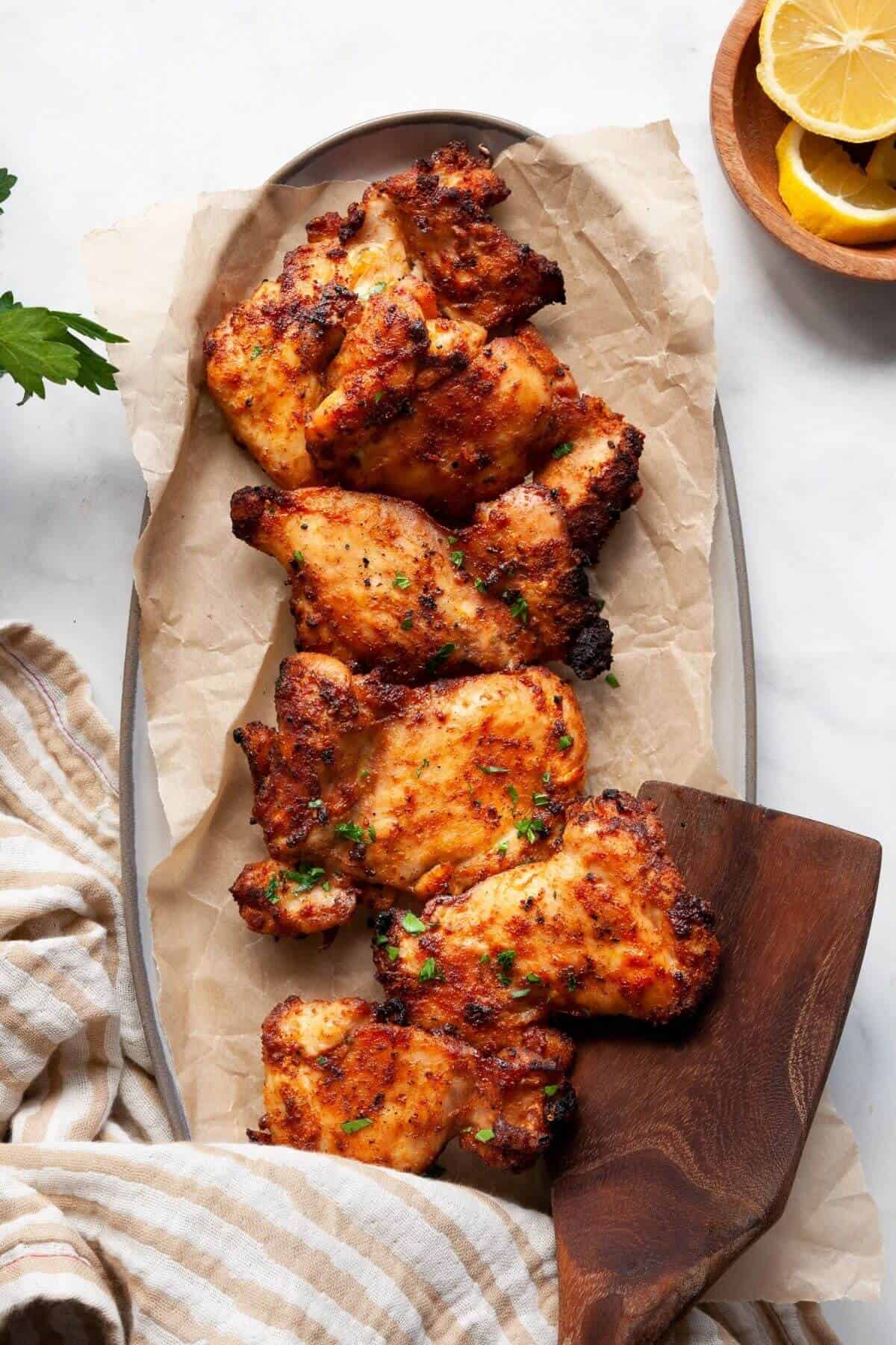 Air fryer boneless and skinless chicken thighs on a plate with parsley and lemon.