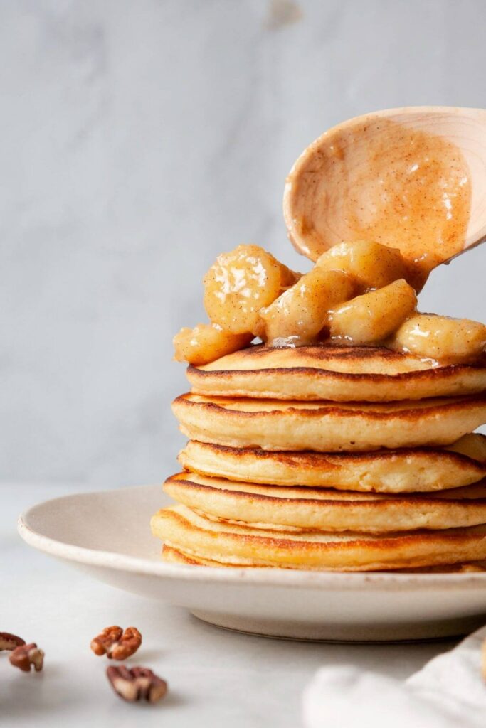 spooning homemade banana foster sauce onto fluffy pancakes stack