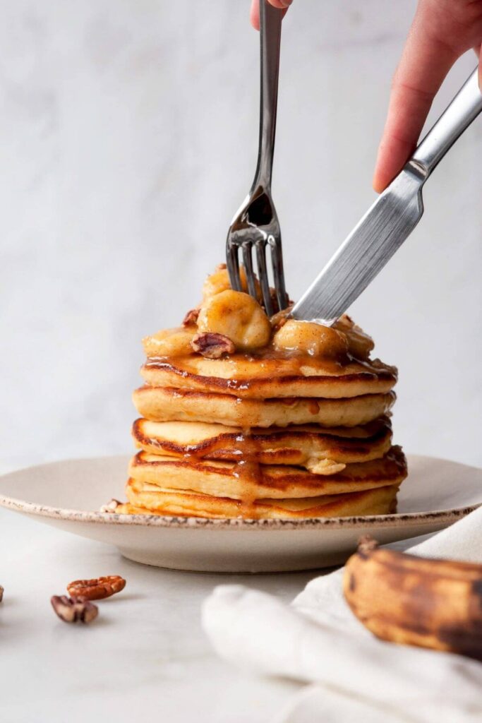 cutting into a stack of banana foster pancakes
