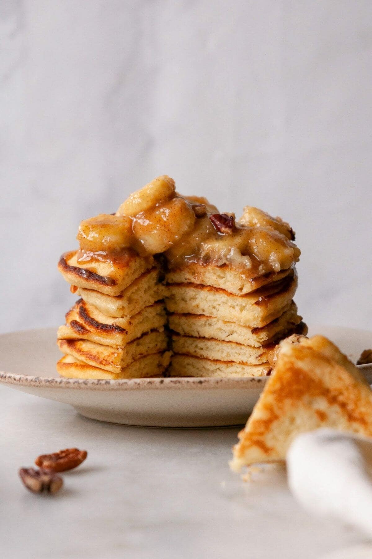 Cutting into stack of caramelized banana foster pancakes to show super fluffy inside texture.