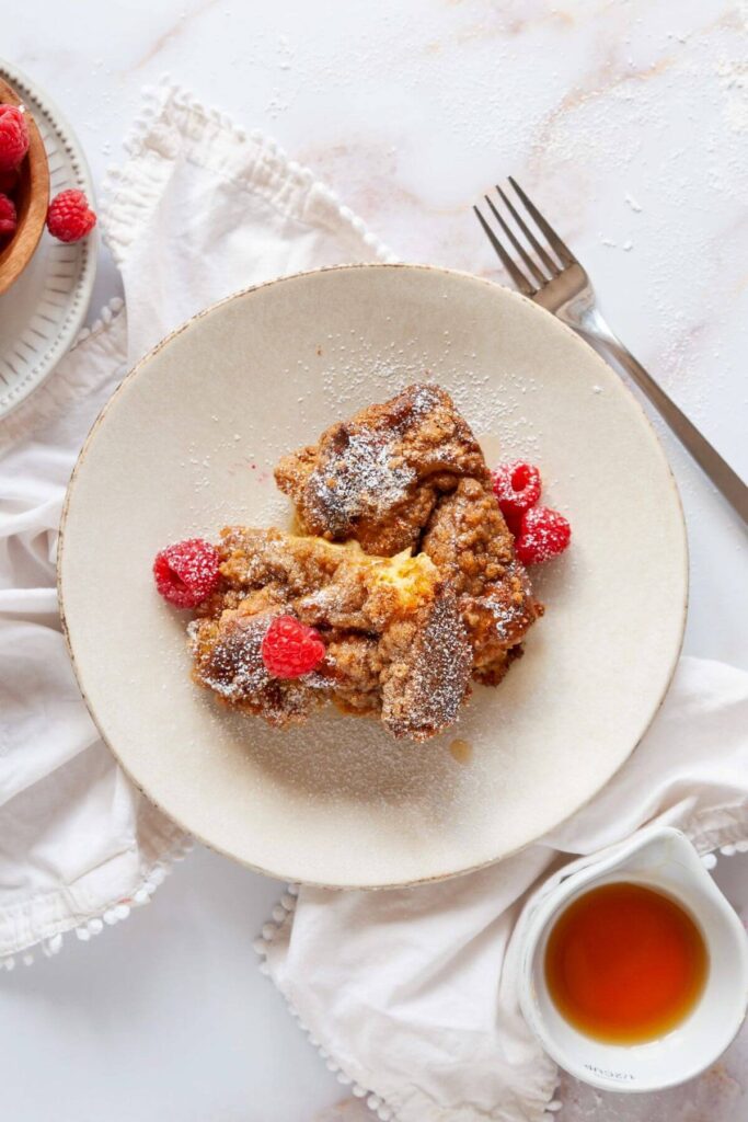 two slices of Brioche French Toast Casserole with rasberries and powdered sugar on a plate