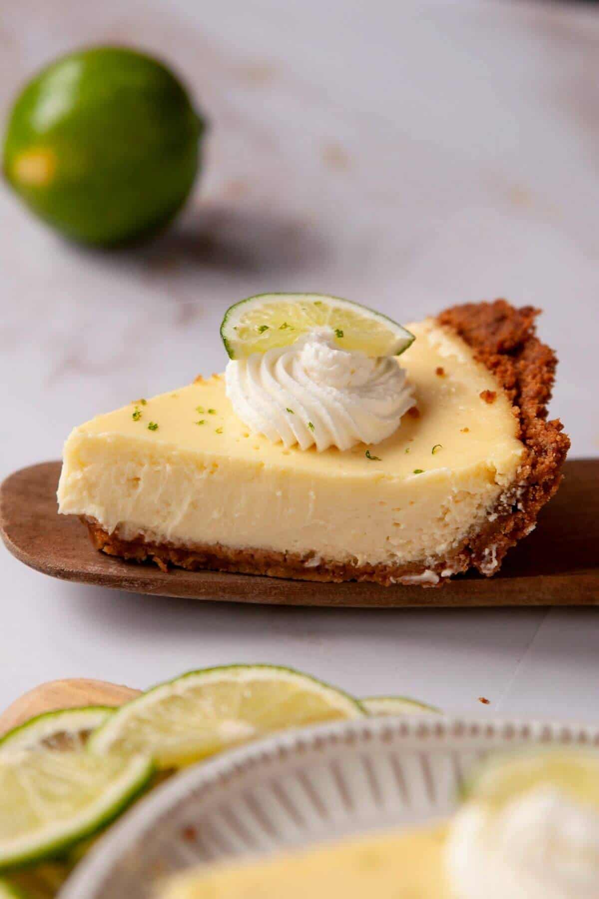 A slice of gluten-free key lime pie with a buttery graham cracker crust, topped with whipped cream and a lime wedge.