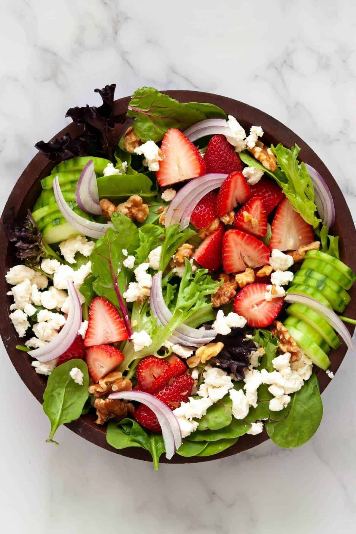 Undressed mixed green strawberry goat cheese salad in a bowl.