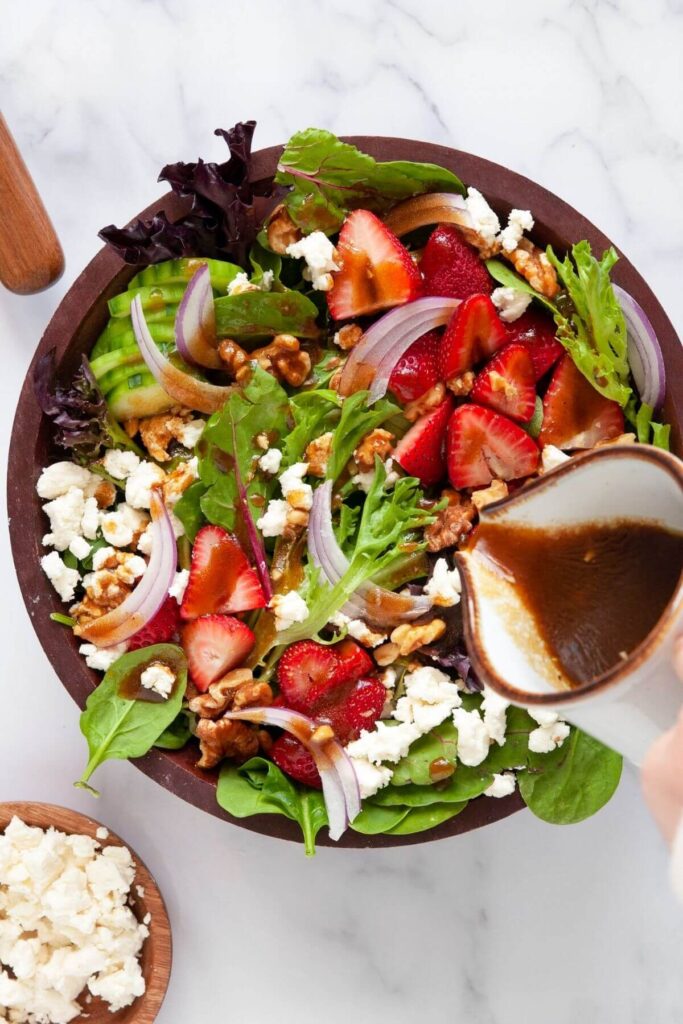 pouring healthy balsamic vinaigrette on strawberry goat cheese salad with onions and cucumbers