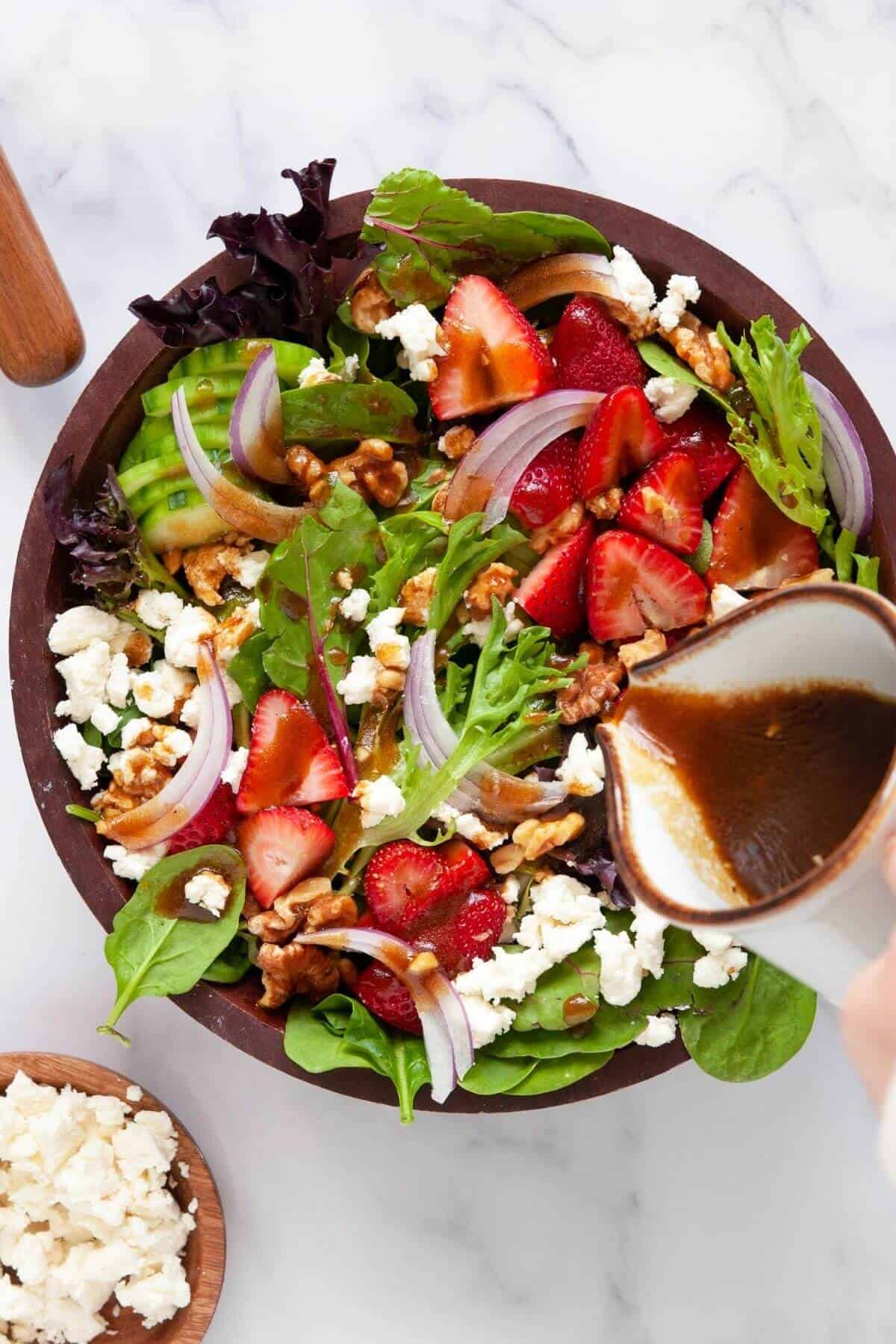 Pouring healthy balsamic vinaigrette on strawberry goat cheese salad with walnuts and cucumbers.