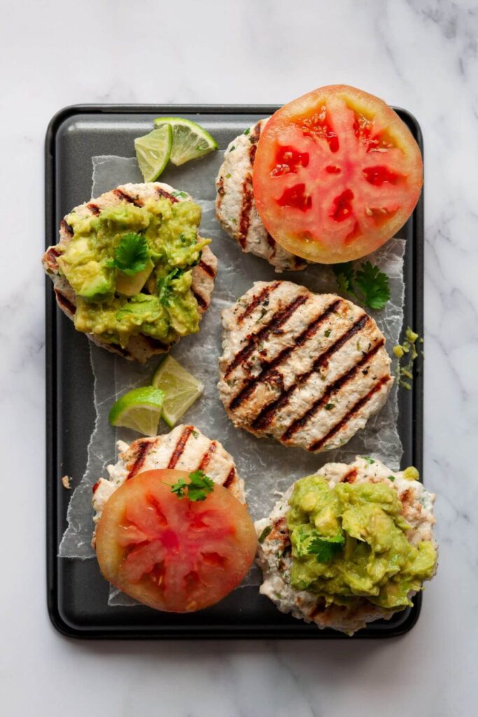 five cilantro lime chicken burgers on plate topped with tomato and guacamole