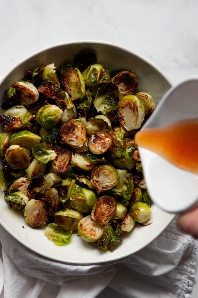 pouring homemade honey sriracha sauce on top of crispy brussel sprouts