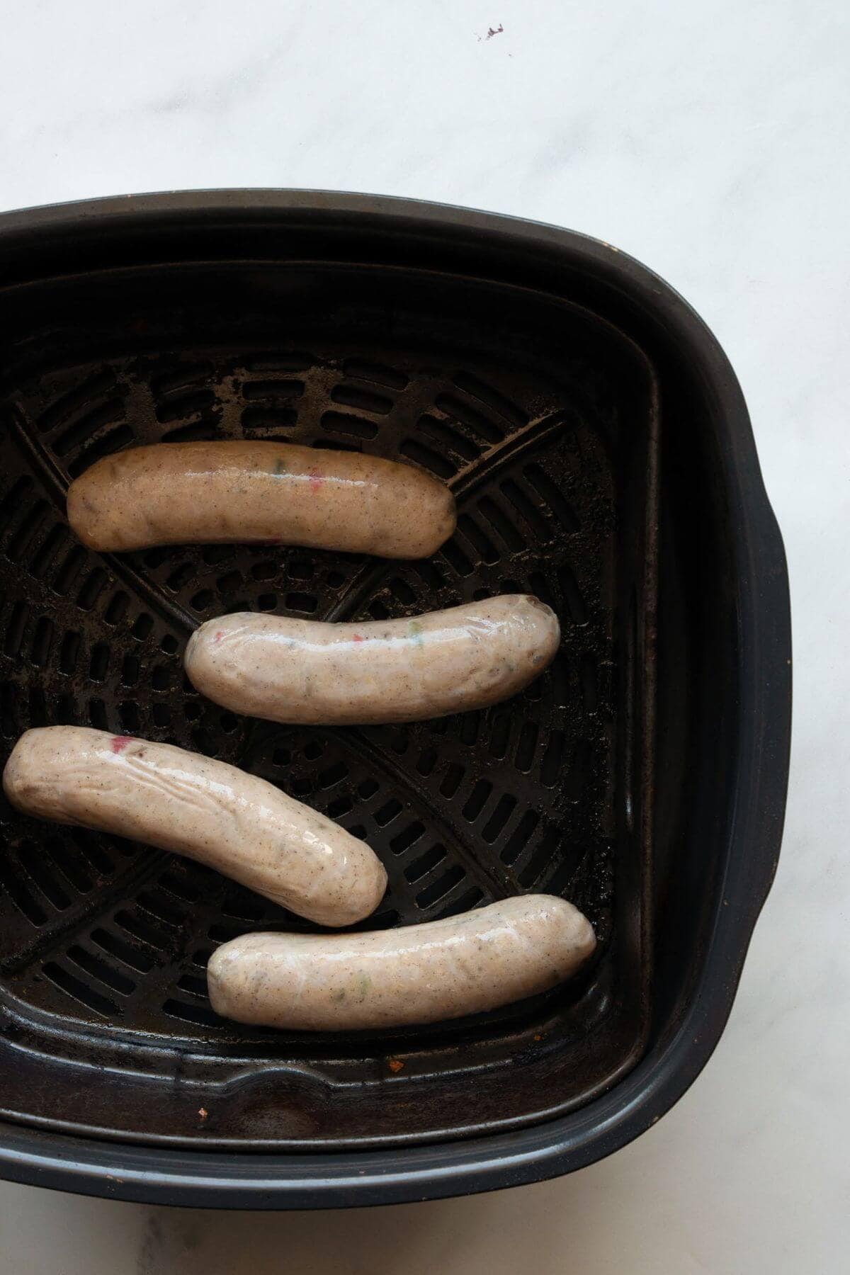 Uncooked chicken sausage links arranged in a single layer in a black air fryer basket.