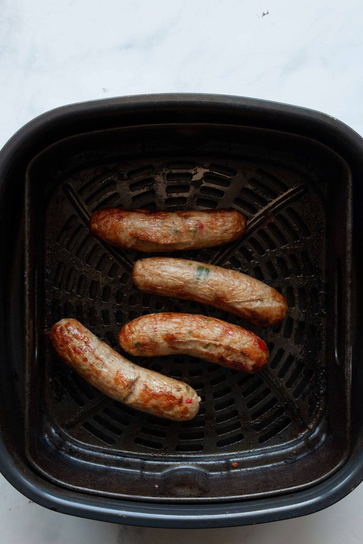Perfectly cooked browned chicken sausages in a black air fryer basket.