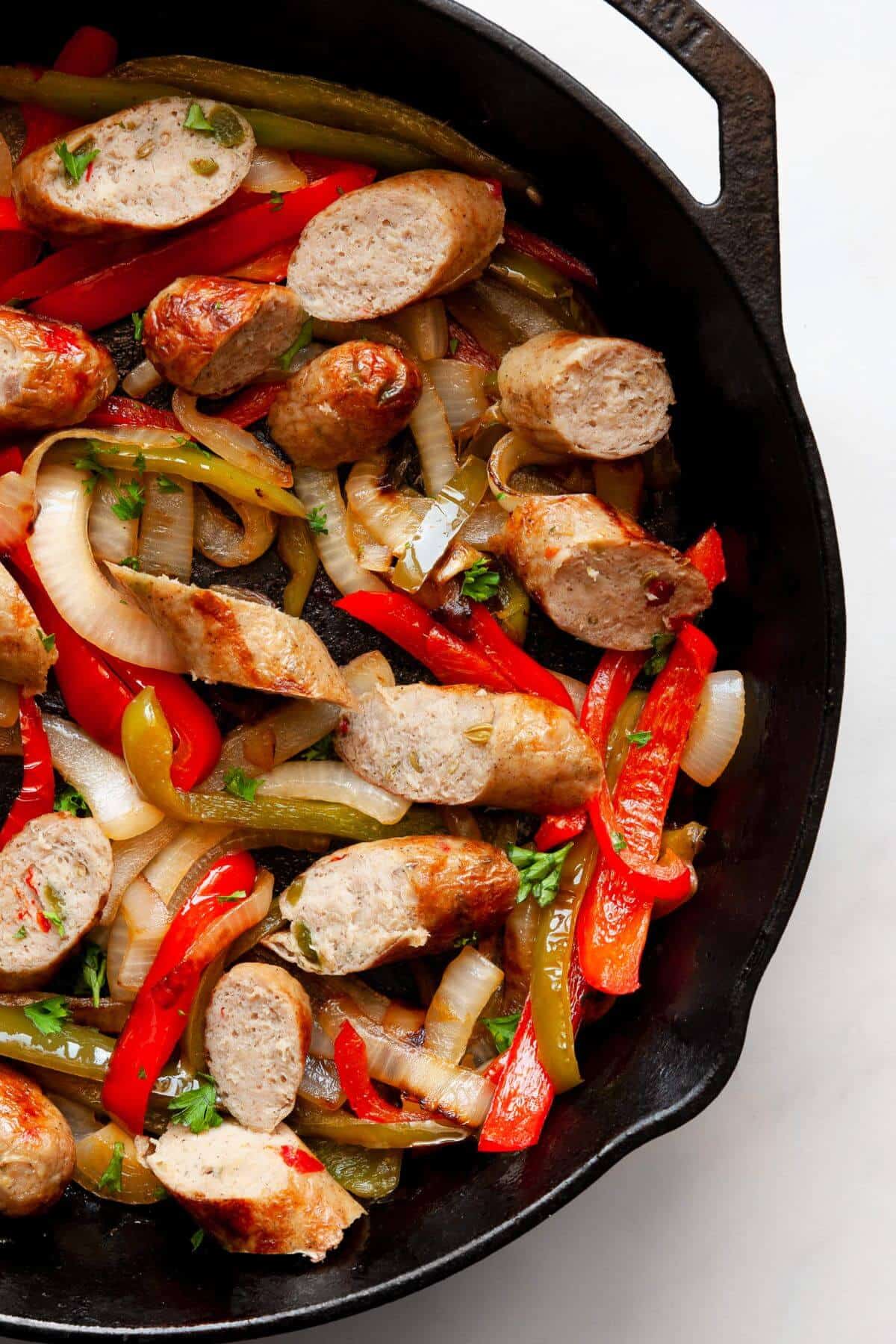 Sliced air fryer chicken sausages with red and green peppers and onions in a cast iron skillet.