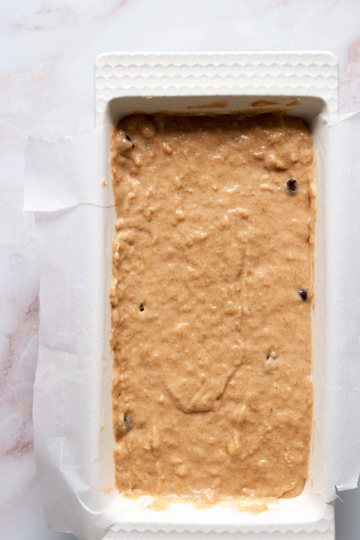 Dairy-free banana bread batter poured into a parchment-lined loaf pan before baking.