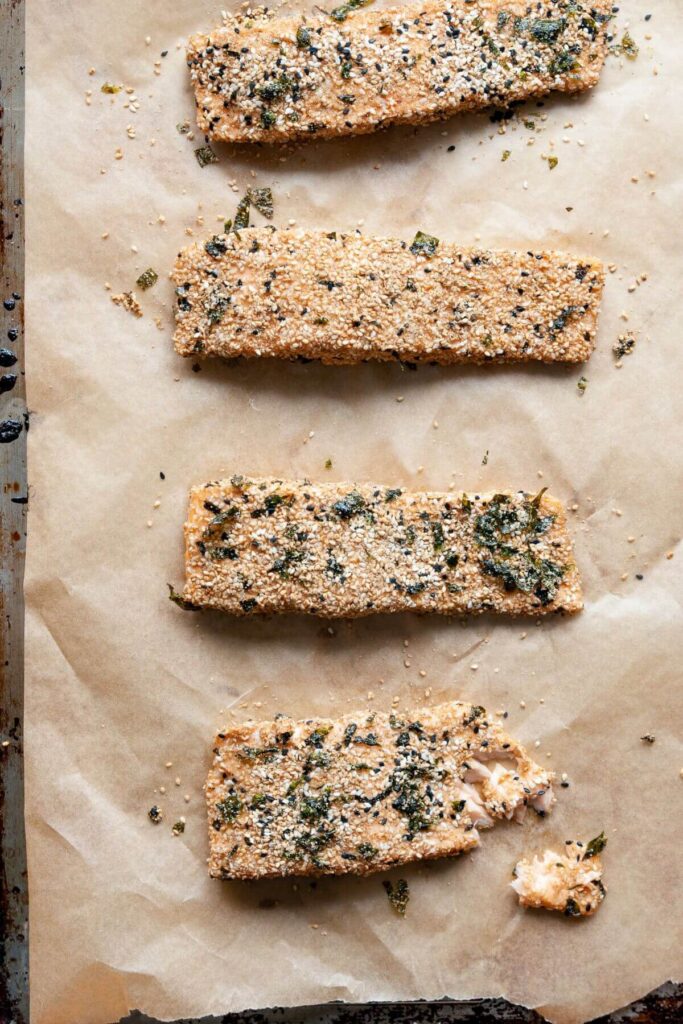 four pieces of cooked furikake crusted salmon on a baking sheet