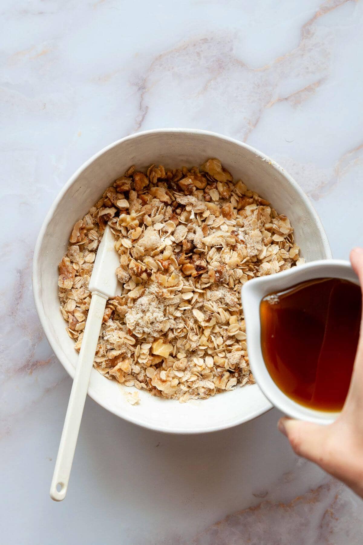 Maple syrup being poured into the oat and walnut crumble topping.