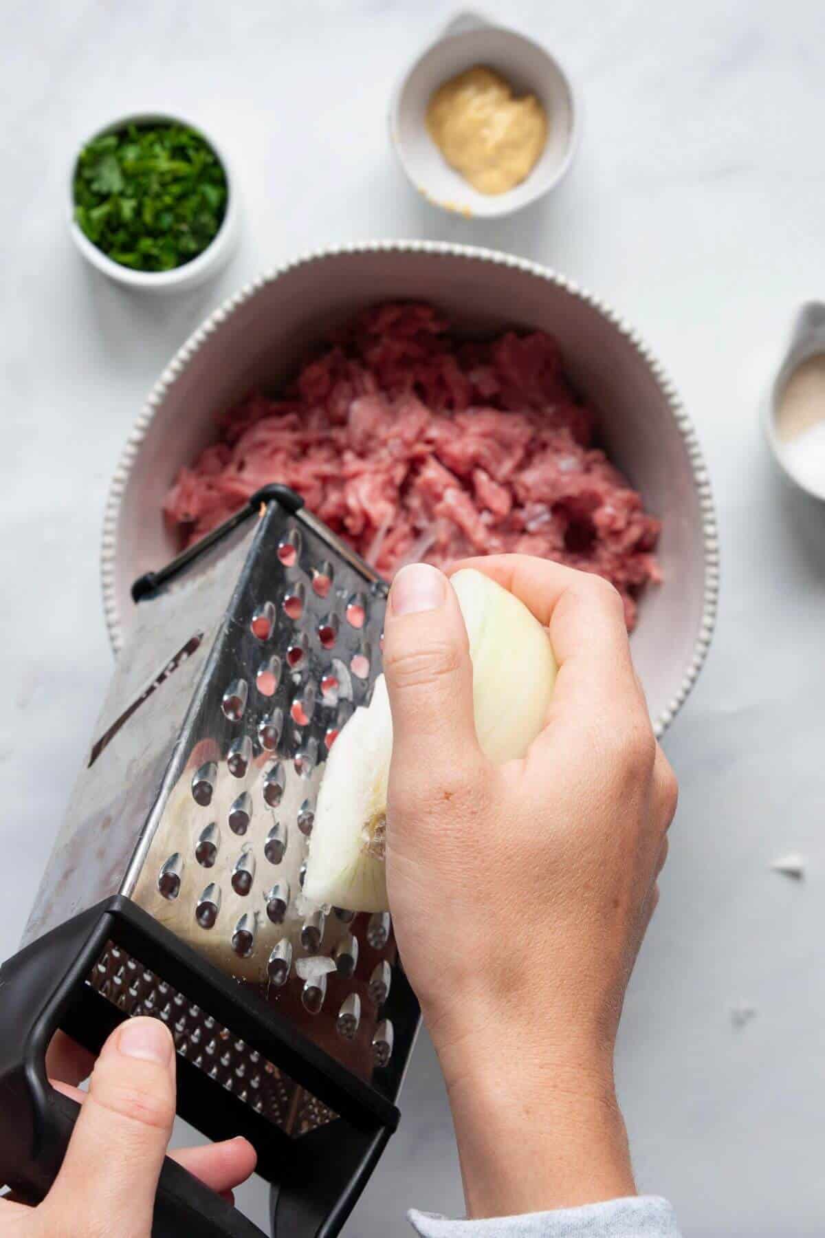 Hand grating yellow onion directly over a bowl of ground turkey using a box grater.