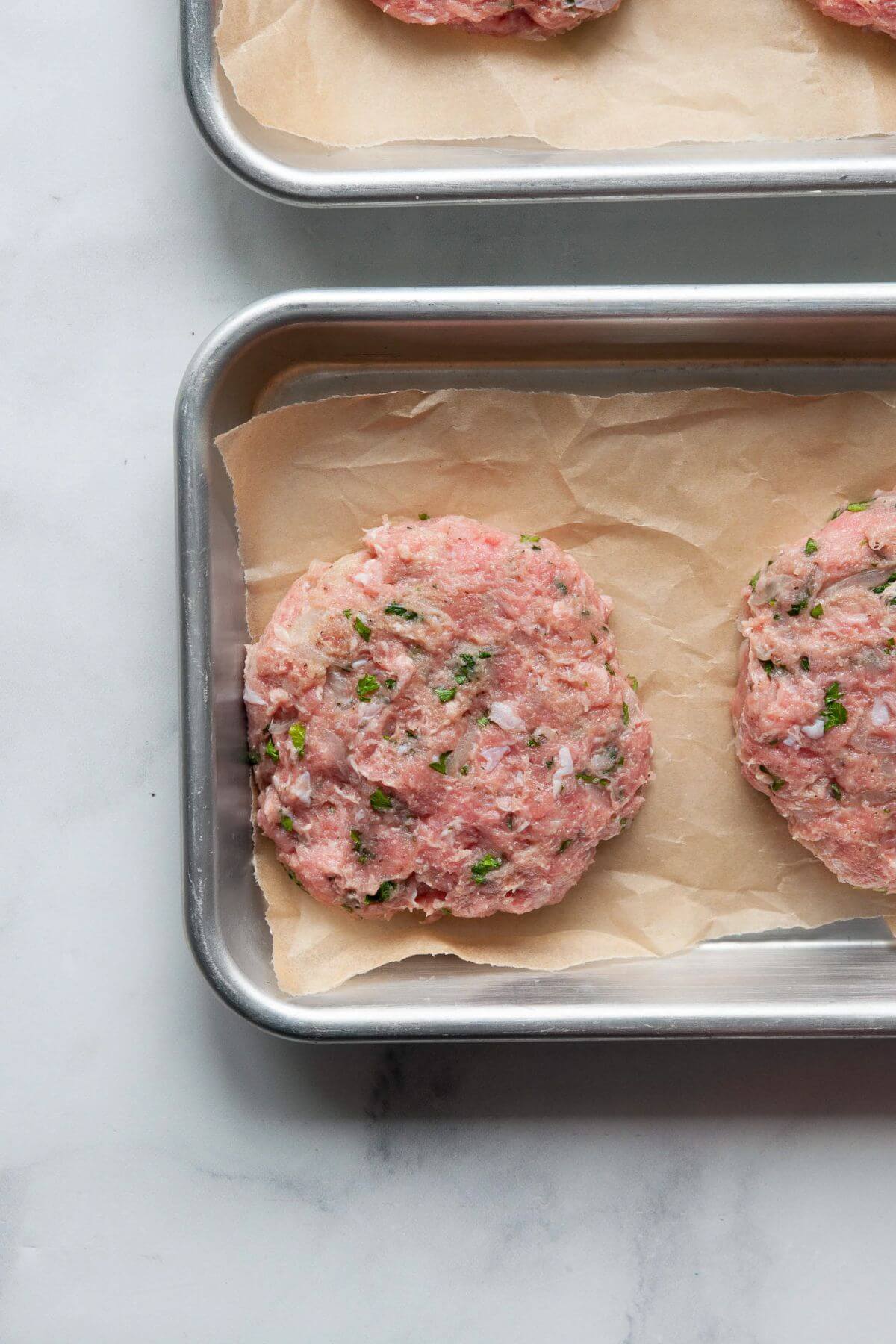 Four raw turkey burger patties shaped on a parchment-lined sheet pan, ready to grill.