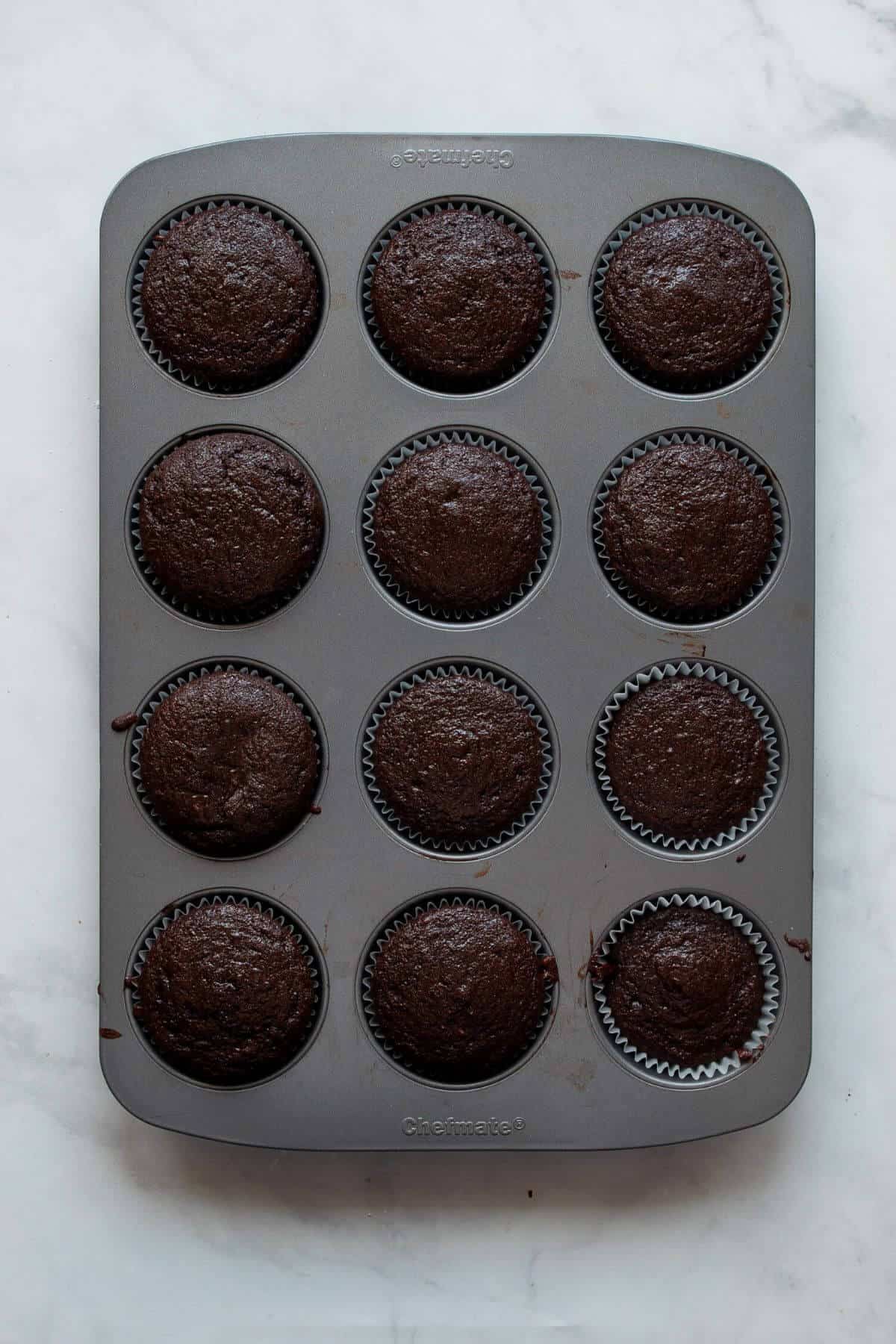 Baked gluten-free chocolate cupcakes cooling in a muffin tin.