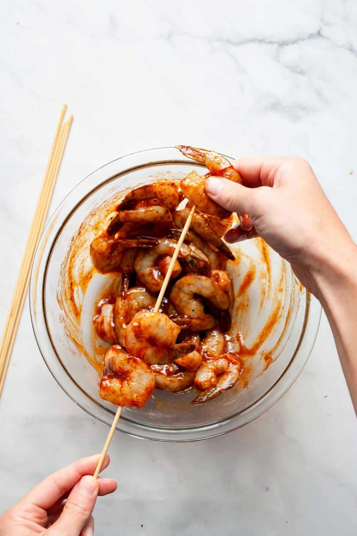 Threading BBQ sauce coated shrimp onto a wooden skewer.