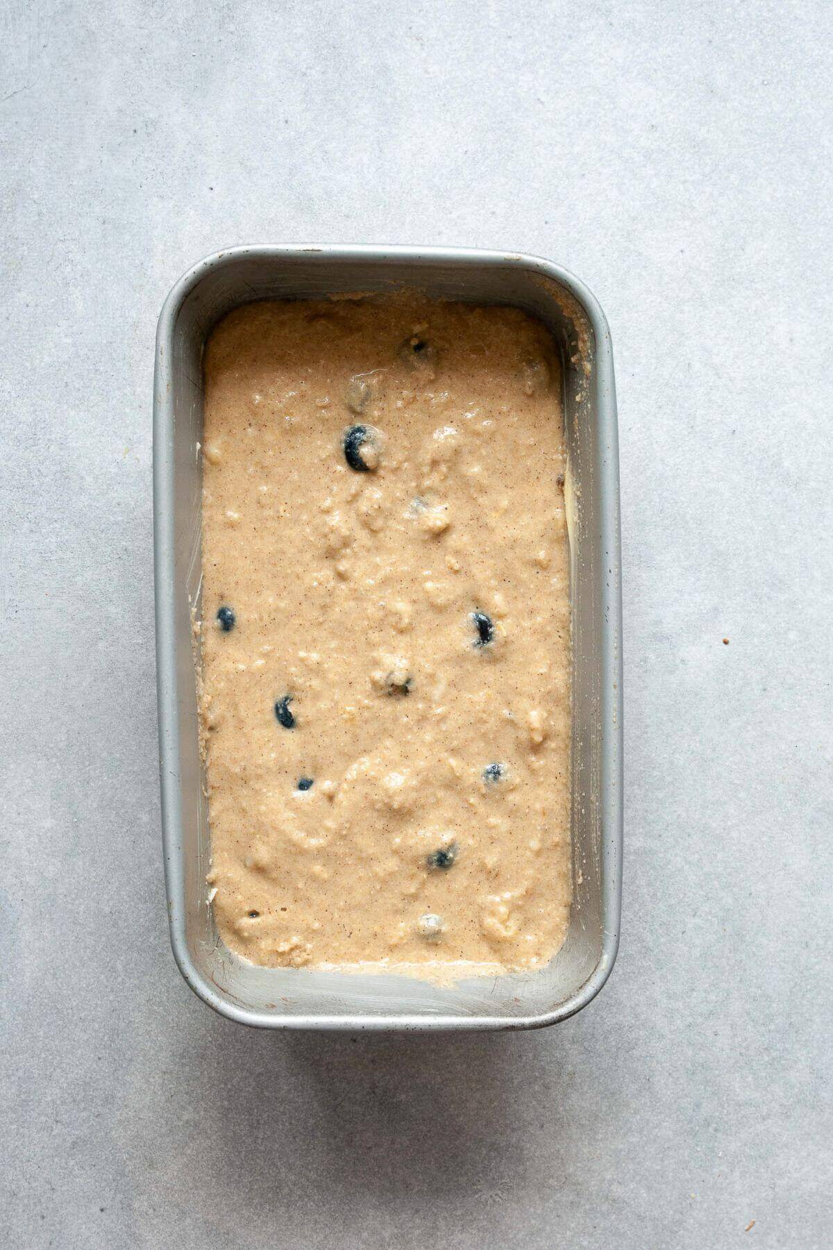 Fresh blueberries folded into banana bread batter with a spatula in a glass mixing bowl.