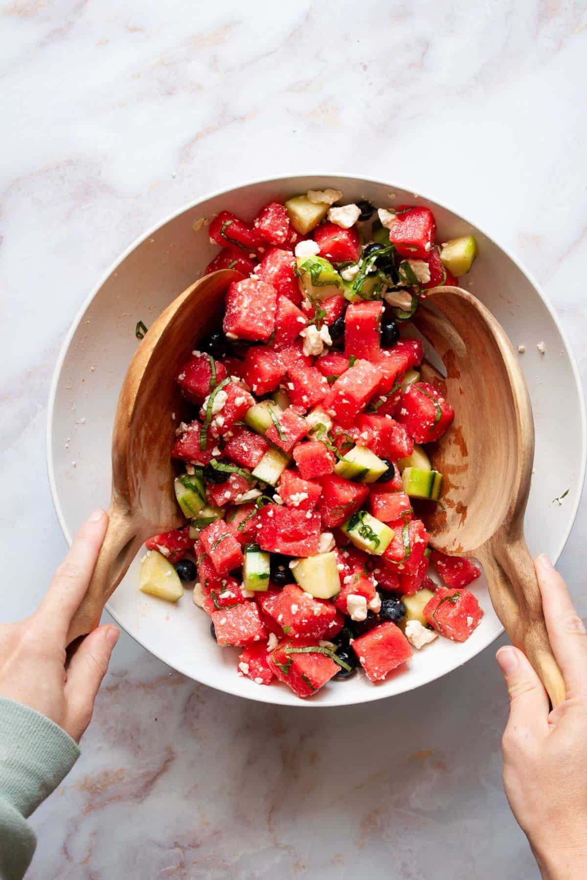 Tossing refreshing watermelon feta salad with wooden salad spoons.