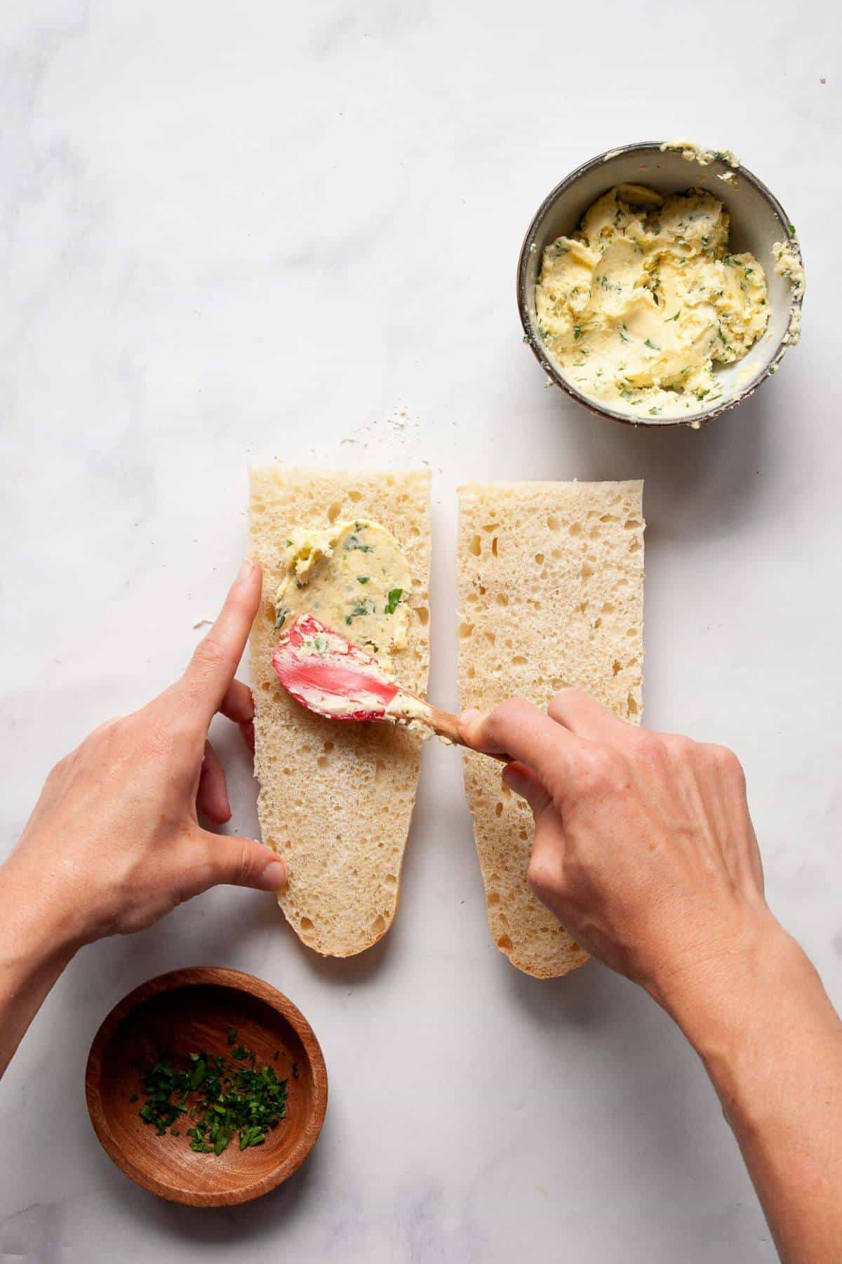 Spreading homemade garlic butter on a baguette slice.
