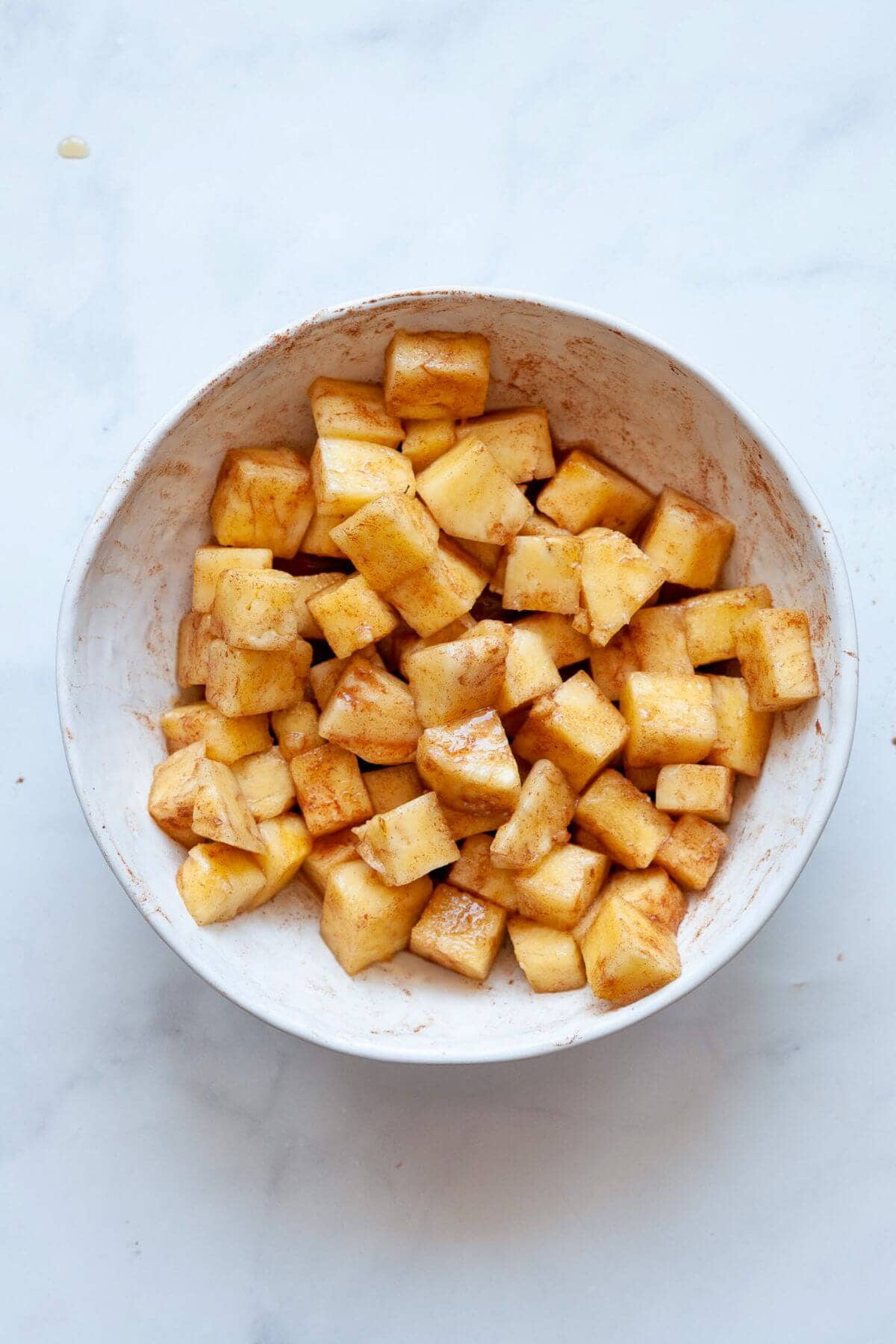 Tossing pineapple so it is fully coated in cinnamon and maple syrup before air frying.