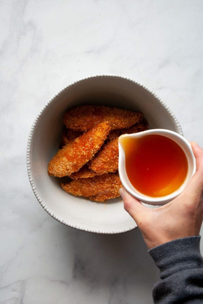 pouring hot honey sauce on top of crispy chicken tenders