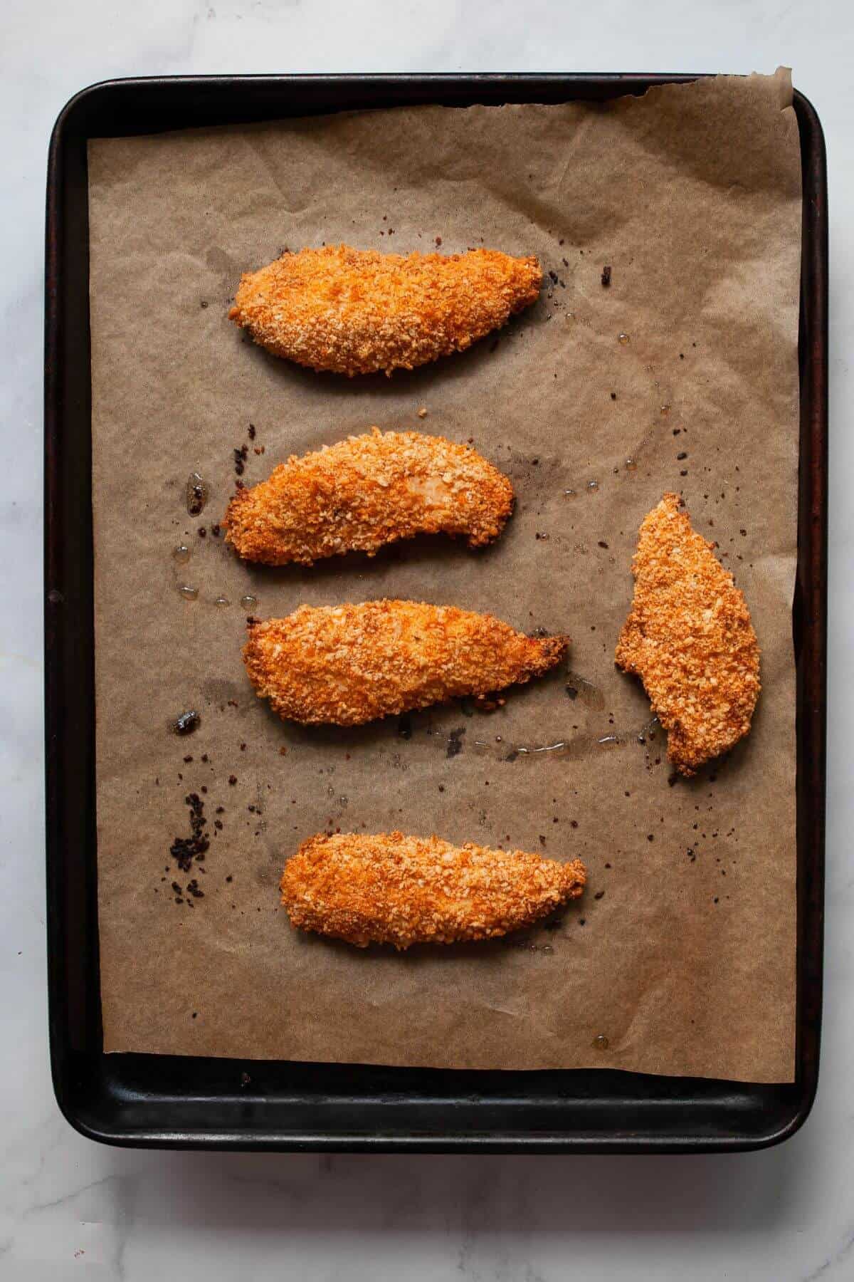 Baked crispy chicken tenders golden brown on a parchment-lined baking tray.
