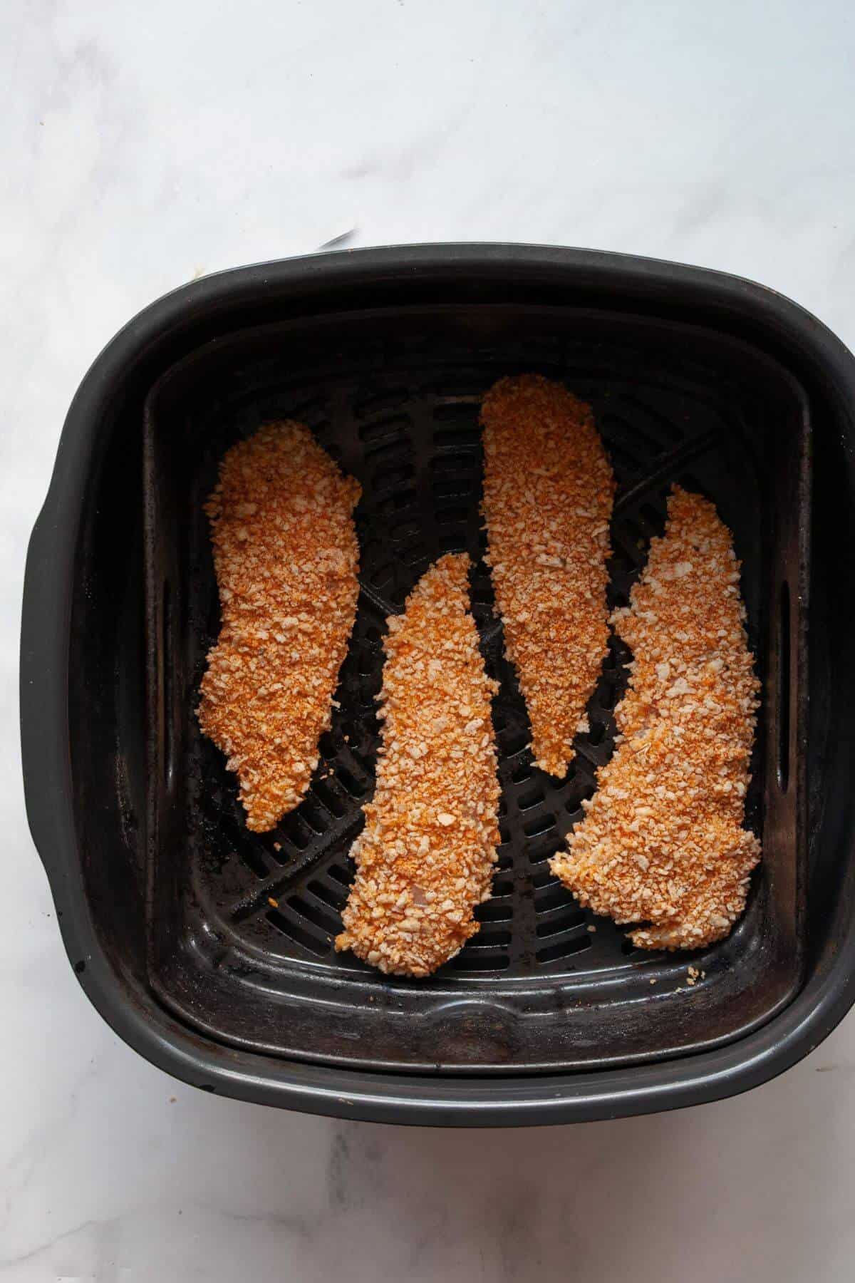 Uncooked breaded chicken tenders arranged in an air fryer basket ready to cook.