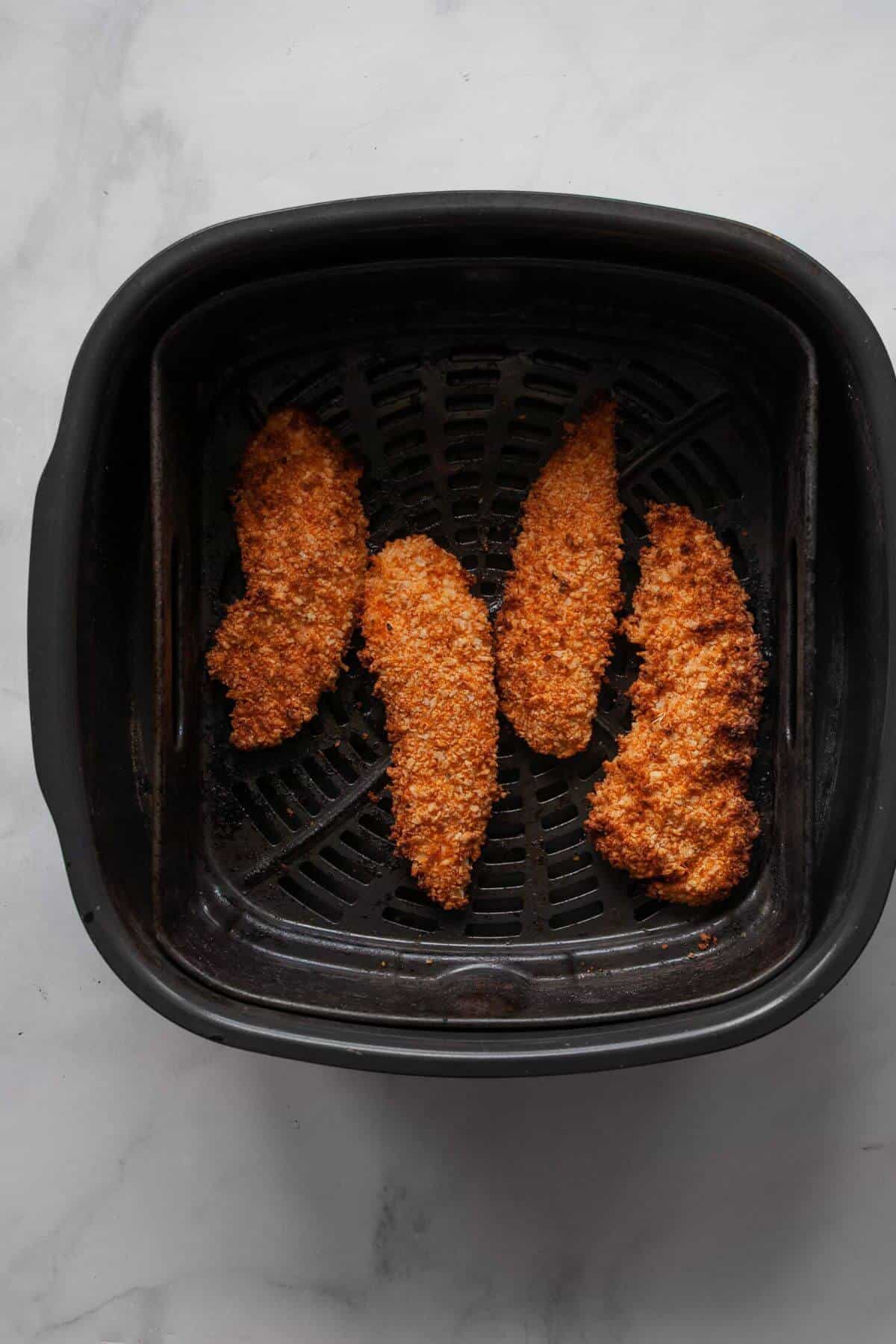 Golden crispy cooked chicken tenders in an air fryer basket.