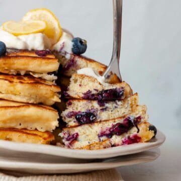 Stack of fluffy lemon blueberry pancakes topped with Greek yogurt, lemon slices, and blueberries.