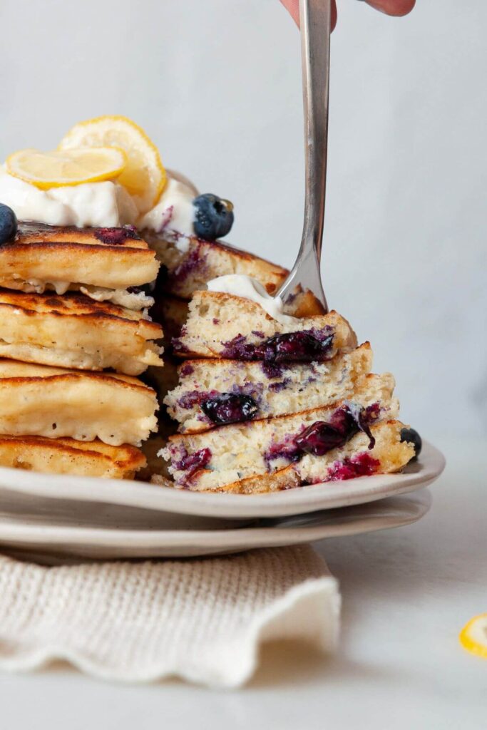 cutting into lemon blueberry pancakes to show soft and fluffy texture