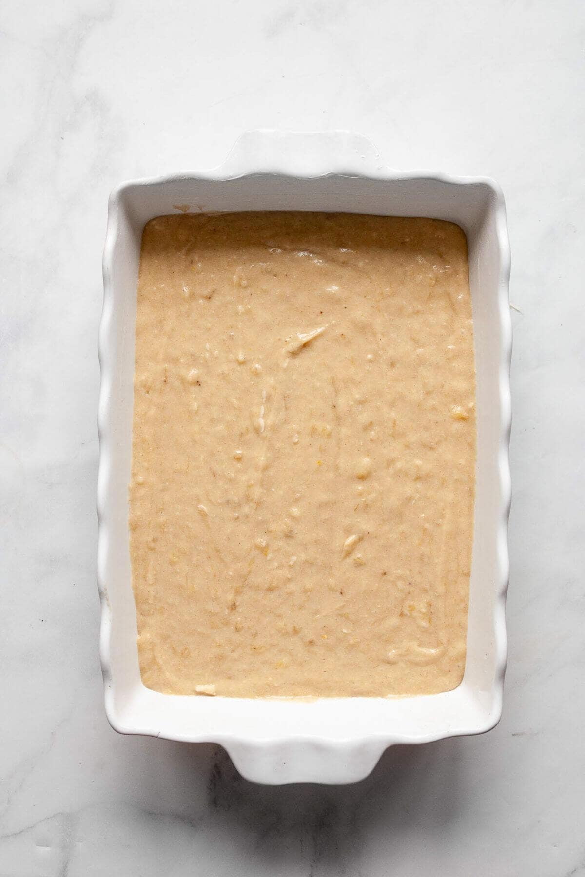 Gluten-free banana cake batter poured into a parchment-lined 9x13 baking pan before baking.