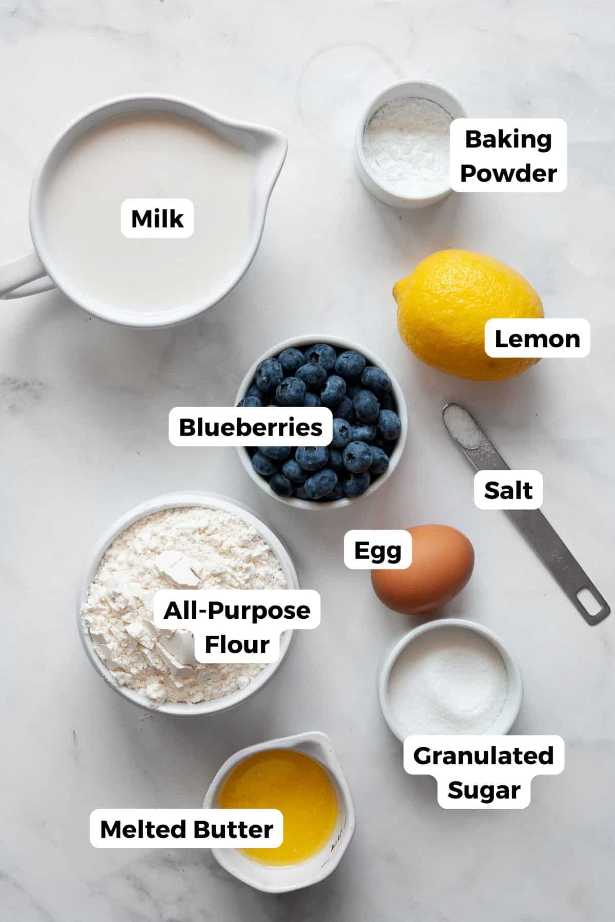 Ingredients for lemon blueberry pancakes, including flour, oat milk, egg, lemon, blueberries, sugar, butter, baking powder, and salt.