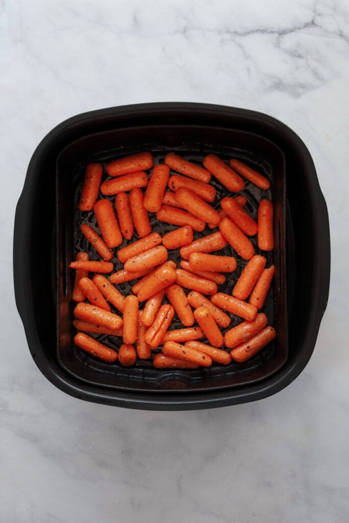 seasoned baby carrots in air fryer basket before cooking