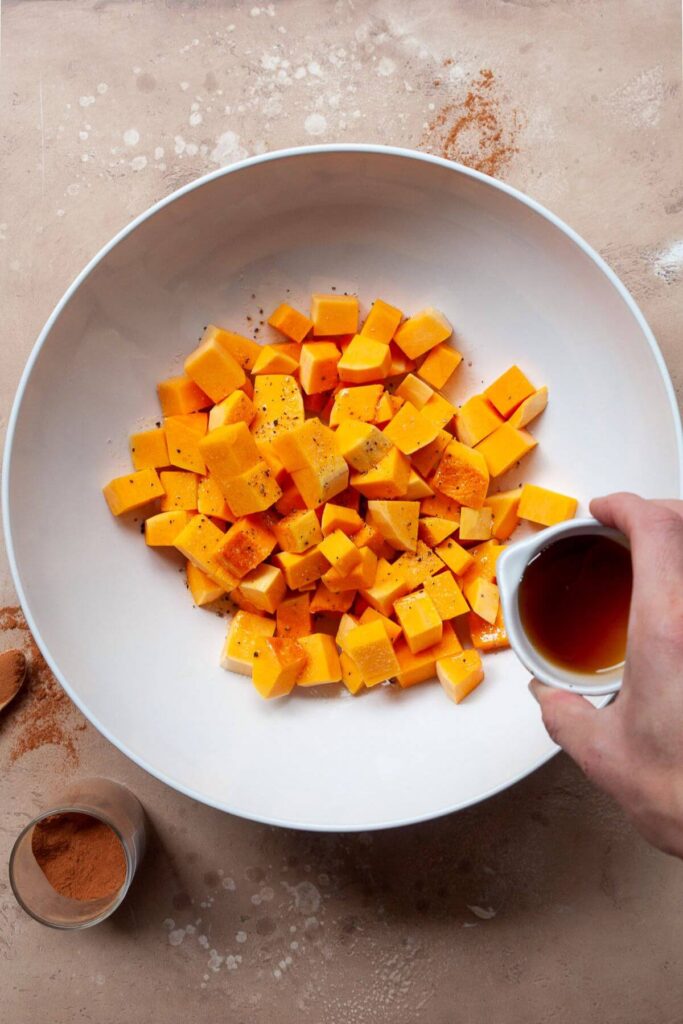 pouring maple syrup on top of butternut squash cubes