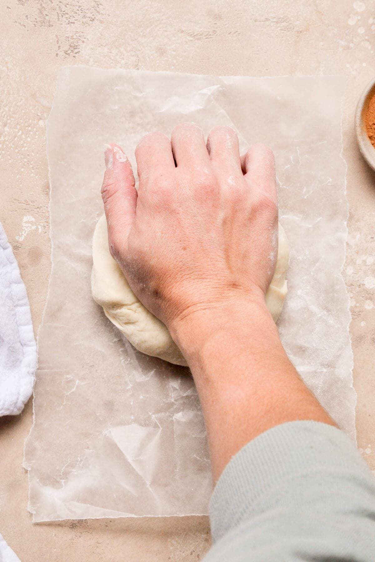 Hands kneading cinnamon roll dough on a floured surface.